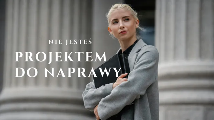 Kobieta w szarym płaszczu z teczką na tle kolumn